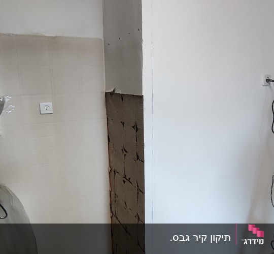 קיר עם אריחים שבורים וכלי עבודה על הרצפה